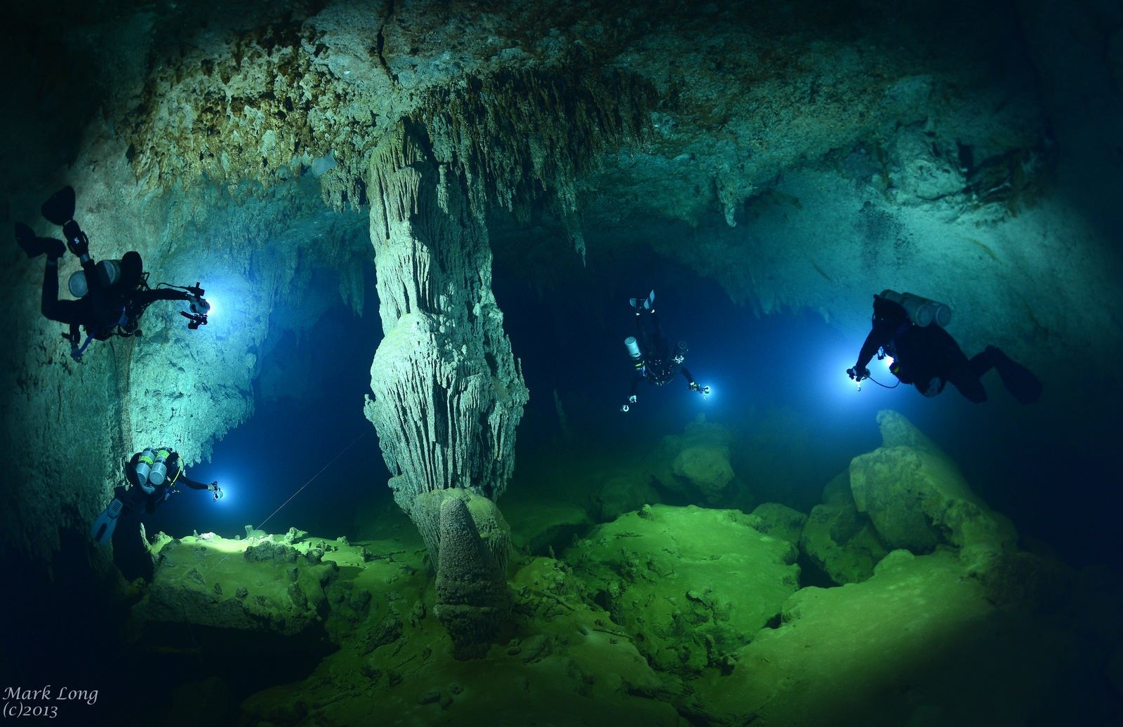 Divers beside a towering limestone column in Giant Cave, Belize